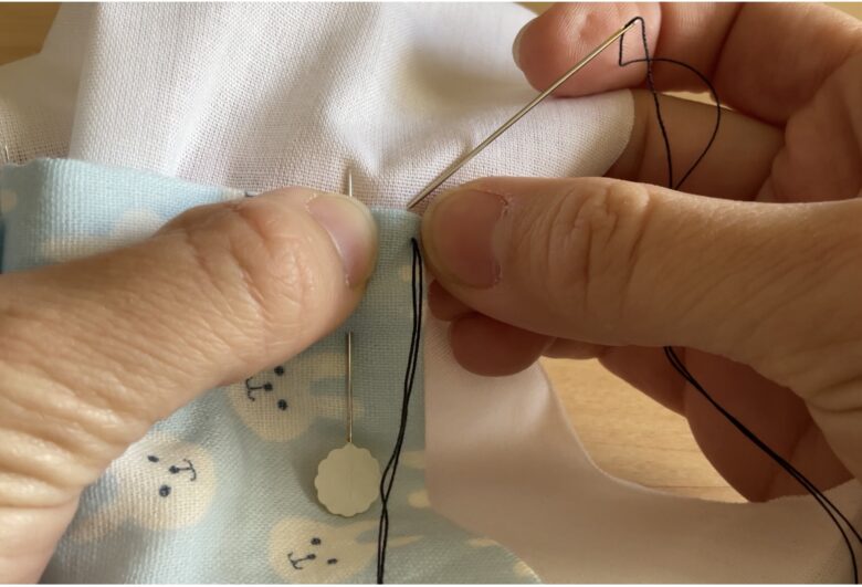 針目が垂直になるように、真上に針を入れ、土台布をすくって、アップリケ布（手前の布）の端に出します。